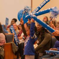 Image of people in audience. Young child showing excitement holding GVSU noisemakers